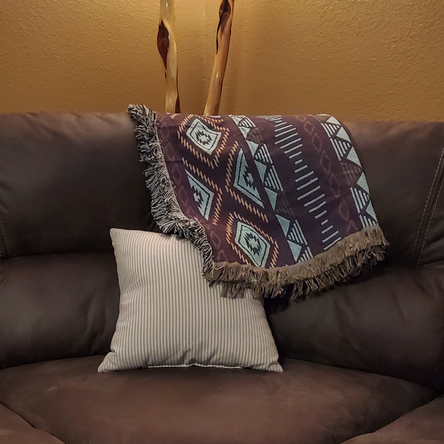 A sofa blanket with a geometric Aztec pattern in white, tan, blue & purple colors.