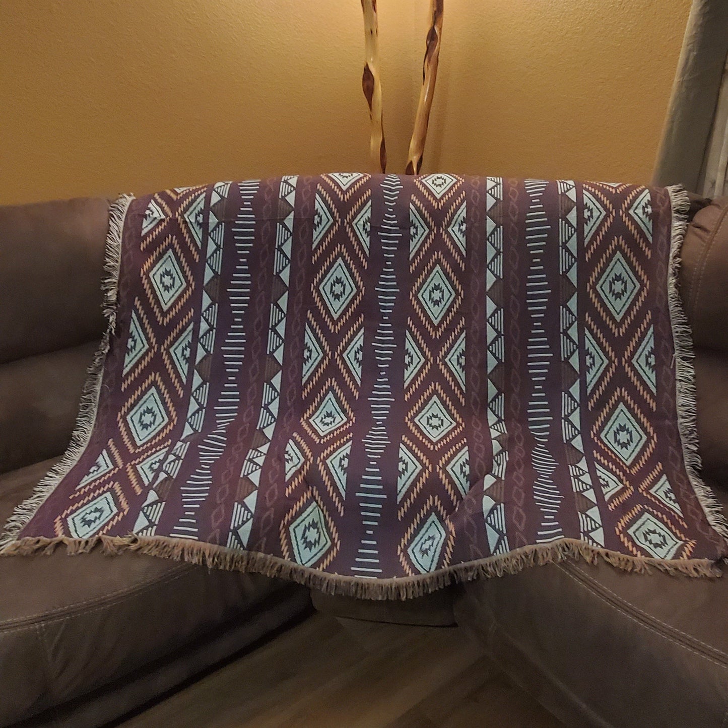 A sofa blanket with a geometric Aztec pattern in white, tan, blue & purple colors.