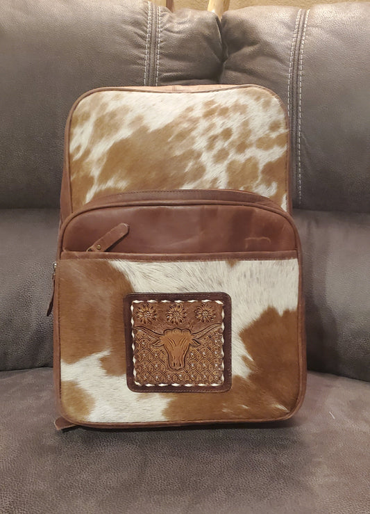 A backpack with a brown leather base and a cowhide patterned top featuring a brown longhorn steer emblem.
